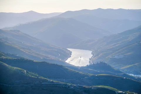 Aerial drone view of a tourist boat on the Douro River surrounded by layered mountain hills and