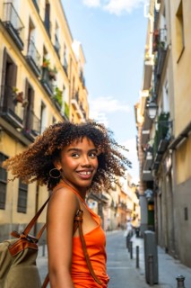 Happy young black woman with curly hair and a backpack looking back and smiling, walking along a