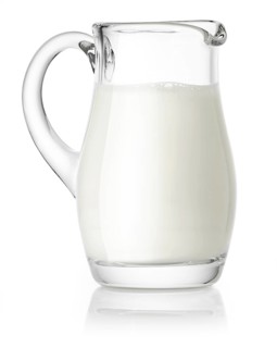 Glass jug filled with milk against a white background, studio shot