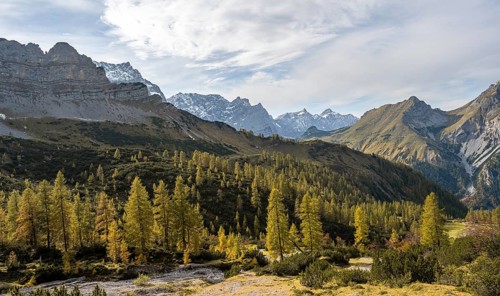 Mountain panorama with steep rocky peaks, yellow-coloured larches in autumn, hike to the summit of
