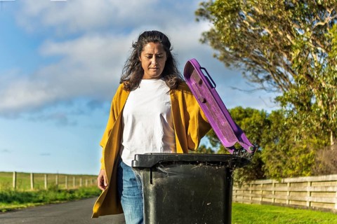 A woman in casual attire handles a bin outside her Australian home. The scenic background