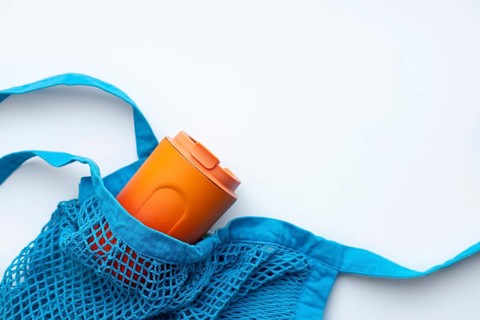Top view of an eco-friendly orange thermo cup tucked inside a bright blue mesh bag, emphasizing