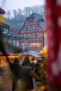 Snow-covered half-timbered house with Christmas market visitors and festive lighting, Christmas