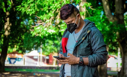 Man with a mask texting with his phone, young man with a mask texting with his cell phone, close up