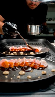 A skilled chef in a restaurant kitchen artfully applies a rich sauce to a gourmet dish. The elegant