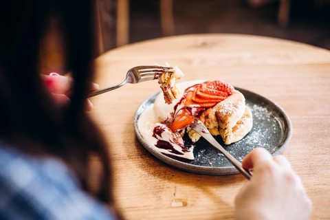 A woman enjoys a delicious japanese pancakes topped with fresh sliced strawberries and cream. The