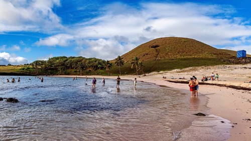 People playing and relaxing on a beach lined with palm trees and hills, the landscape of Easter