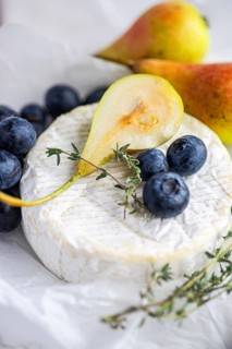 A close up image showcasing creamy Brie cheese paired with ripe, juicy pears and fresh blueberries.
