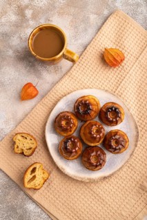 Golden caramelized Canele cookies dessert, cup of coffee, on brown concrete background with beige