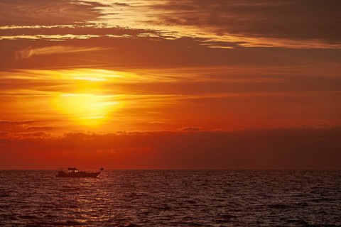 A boat sails across the sea at sunset, the sky is colored in bright orange and red, Cyprus