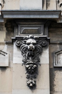 Sculptural lion head as an architectural ornament and relief on a stone house façade, vertical