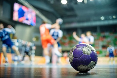 The handball ball laiyng on the parquet and handball match in the background in Lubin, Poland