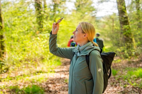 Smiling woman holding a leaf surrounded by spring-like forest landscape, Heckengäu nature tour,