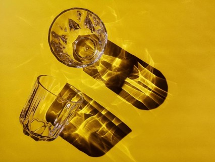 Two glass glasses with faces on a yellow background in hard light with shadows. Two clear glass