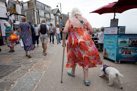 Elderly woman from behind, on stick, running with dog, St Ives, Cornwall, England, Great Britain,