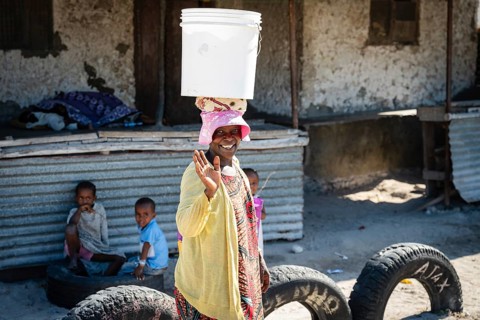 PAJE, ZANZIBAR - OCTOBER 18, 2025: A smiling local woman carries a white bucket on her head while
