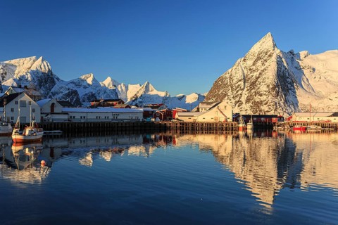 Snow-covered mountains reflected in fjord at sunrise, village, winter, Reine, Moskenesoya, Lofoten,