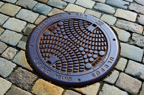 Round manhole cover with geometric pattern on cobblestones, Bergen, Vestland, Norway