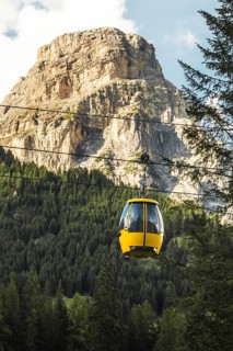 Dolomites, Italy - 27th july, 2026: Colfosco yellow cable car gondola lift ascending over lush