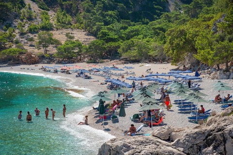 Apella beach, with many people, parasols and surrounding forest, Apella beach, Karpathos, Greece