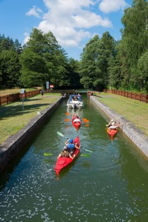 Kayakers and a boat enjoying a summer day on a narrow canal with green surroundings, Sluza Paniewo,