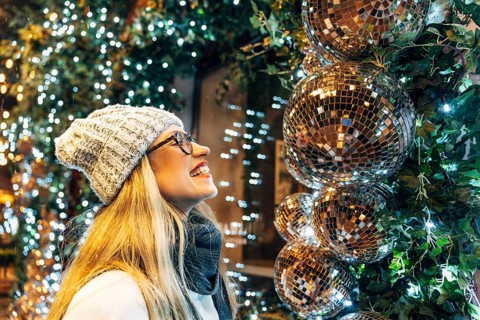 Young woman enjoying festive lights and decorations. A person wearing a white knitted hat, glasses