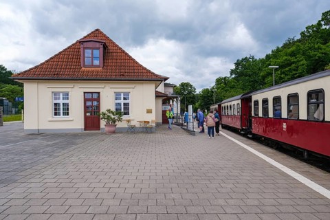 A small train station with a nostalgic train and people on the platform under cloudy sky, Bad