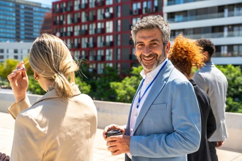 Smiling businessman holding coffee cup and wearing an id badge, looking at camera while attending a