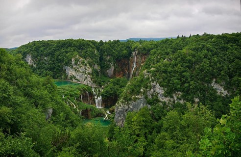 Panoramic view of a waterfall surrounded by thick green forest and rivers under a cloudy sky,