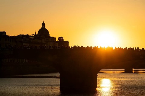 Crowd of people on a bridge over the Arno at sunset, back light, silhouette of a dome in the