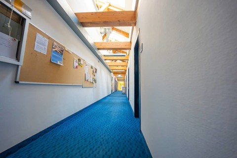 A long corridor with blue carpet and notice boards on the walls under wooden ceiling, old disused