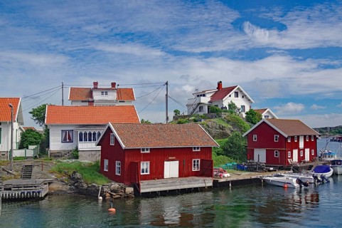 Small coastal village with red and white wooden houses on the shore, boats in the water, blue sky,