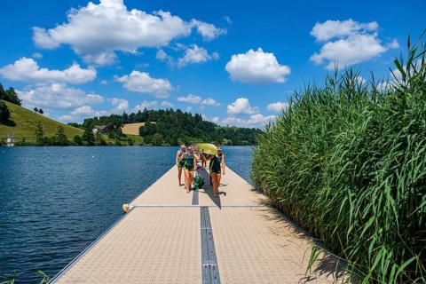 Rowers on a jetty carrying a boat surrounded by reeds and a blue sky, Rotsee, Canton of Lucerne,