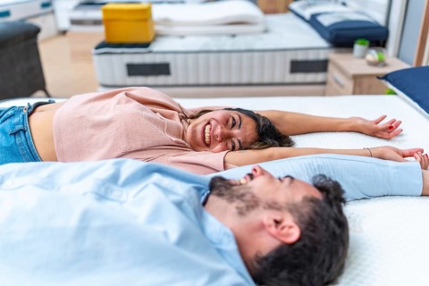 Young couple lying on a mattress in a furniture store, testing comfort and smiling as they pick the