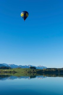 A hot air balloon flies high above a lake with a wide view of the mountains, Lechstausee,