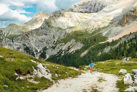 Female hiker with backpack walking dirt trail green alpine meadow majestic mountain peaks