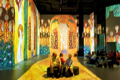 Visitors in an immersive exhibition, digital art, colorful projections on walls and floors,