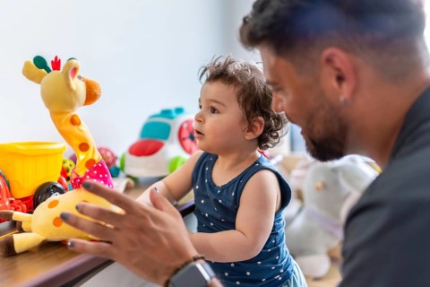 Father and baby son engaging in playful interaction at home, with the toddler happily reaching for