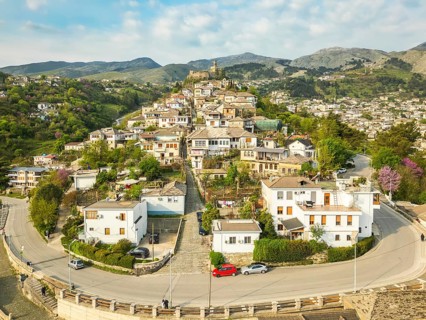 Aerial panoramic view massive stone Gjirokaster Castle on hilltop, surrounded by historic Stone