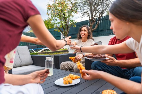 Family gathered around a garden table smiling and sharing breakfast pastries and drinks during a
