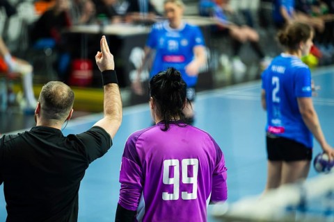 A handball referee signals a two-minute penalty while standing near players during a professional