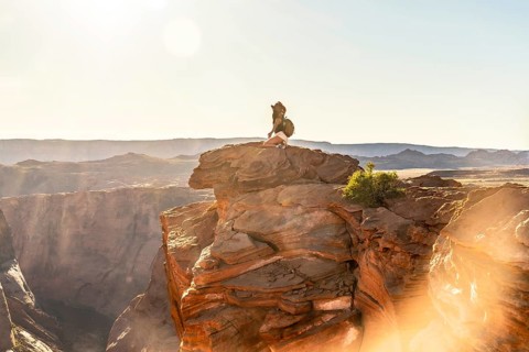 Woman traveler sits on a rock overlooking a vast horseshoe bend canyon at sunset, sunlight warming