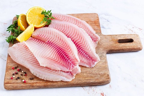 Fresh Tilapia fillet, on a wooden chopping board, with lemon and herbs, ready to cook in the