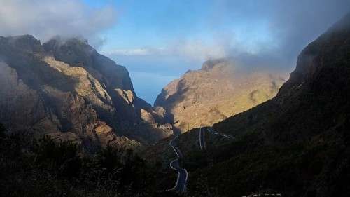 Dramatic mountain scenery with winding road and mystical fog illuminated by sunbeams, Masca,