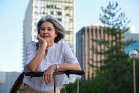 A mature woman with gray hair and a content expression enjoys a leisurely moment on her scooter in
