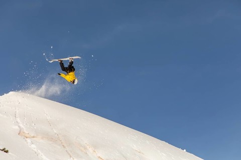 A snowboarder performs an exhilarating trick in the backcountry, surrounded by pristine powder and