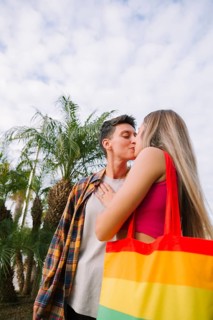 A lesbian couple shares a tender moment outdoors, exuding love and joy. With a rainbow bag as a