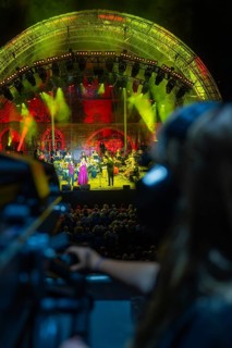 Visitors watch a concert under imaginative lighting with a cameraman in the foreground,