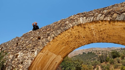 Person on a historic stone bridge looking into the distance surrounded by nature and clear sky,