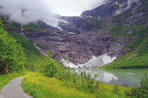 A narrow path leads to a majestic mountain with a waterfall in foggy surroundings, glaciers,